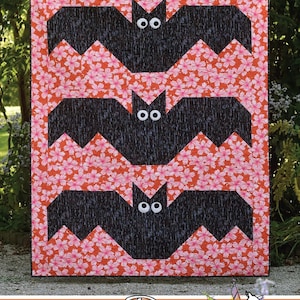 May include: A quilt pattern called "Batty" featuring three black bats with white eyes on a pink and orange floral background. The quilt pattern is by Running Doe Quilts for Villa Rosa Designs.