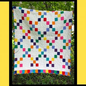May include: A white quilt with a colorful checkerboard pattern of red, pink, blue, green, yellow, and purple squares. The quilt has a rainbow border and is hanging outdoors. The image includes the text "Lollipop" and "Tricia Lynn Maloney Orphan Quilt Designs".
