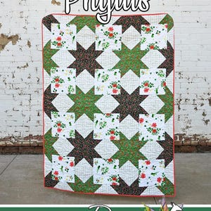 May include: A handmade quilt with a star pattern in green, brown, and floral prints. The quilt features the name "Phyllis" in cursive script. The quilt is from Running Doe Quilts for Villa Rosa Designs.
