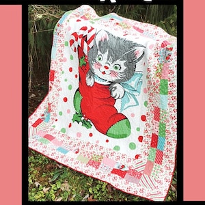 May include: A white, red, and green patchwork quilt with a cute cartoon cat in a stocking. The quilt is on a bed of green grass. The quilt is titled "Whiskers" and is by Tricia Lynn Maloney for Villa Rosa Designs.