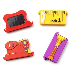 May include: A set of four sewing-themed silicone clips including a red chalkboard-style clip, a yellow measuring tape clip marked with the text Inch 1, a red sewing machine clip, and a purple clip featuring a yellow zipper graphic design.