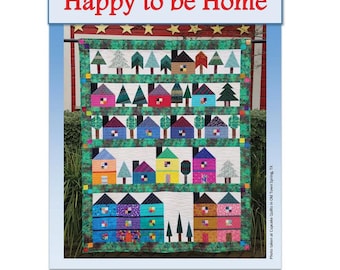 May include: A colourful quilt with a patchwork design of houses and trees. The quilt is titled "Happy to be Home" and is designed by Minay Sirois.