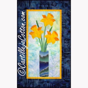 May include: A quilted wall hanging featuring three yellow daffodils in a blue vase. The vase has a layered design of green, blue, and white. The background is light blue and green, framed by a yellow border and a dark blue patterned edge. The text "CastillejaCotton.com" is on the left side.