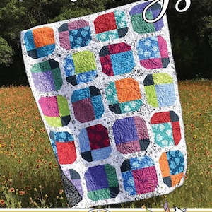 May include: A colorful quilt with the text "June Bugs" and "Running Doe Quilts". The quilt features a patchwork design with squares of various colors, including orange, blue, green, and purple. The quilt is displayed outdoors in a field of flowers.
