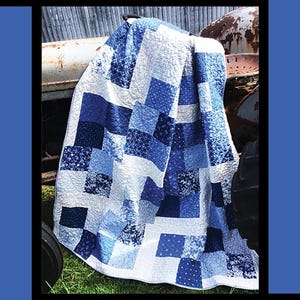 May include: A blue and white patchwork quilt with a farmhouse theme. The quilt is draped over an old rusty tractor. The quilt pattern is called "Farmhouse Blues" and is designed by Tricia Lynn Maloney for Villa Rosa Designs.