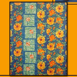 May include: A quilt featuring a floral design in orange and yellow hues against a dark blue backdrop. The word "SUNDANCE" is displayed at the top, with "Villa Rosa Designs" at the bottom. The quilt is framed by orange and blue borders.