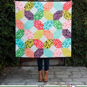 May include: A colorful quilt with a geometric pattern, titled "Asagail" and made by Running Doe Quilts for Villa Rosa Designs.