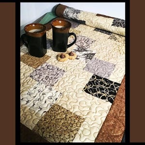 Könnte beinhalten: Ein gesteppter Tischläufer mit einem Patchwork-Design, das Quadrate in verschiedenen Mustern und Farben zeigt, darunter Schwarz, Beige und Braun. Zwei Kaffeetassen und Kekse befinden sich auf dem Läufer. Der Text "Coffee Break" steht oben.