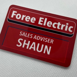 May include: Red name tag with black trim, reading "Foree Electric" in white letters. Below, it says "Sales Advisor" and "SHAUN" in white letters.
