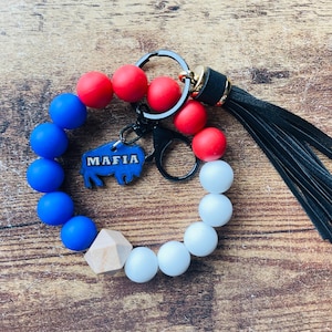May include: A red, white, and blue silicone beaded bracelet with a black leather tassel and a metal keychain with a buffalo charm that says "MAFIA".