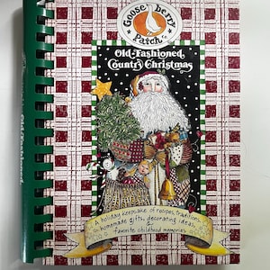 May include: A spiral-bound cookbook titled Old-Fashioned Country Christmas by Gooseberry Patch. The cover features a Santa Claus illustration, a red and white plaid background, and a yellow banner with the text: A holiday keepsake of recipes, traditions, homemade gifts, decorating ideas, & favorite childhood memories.