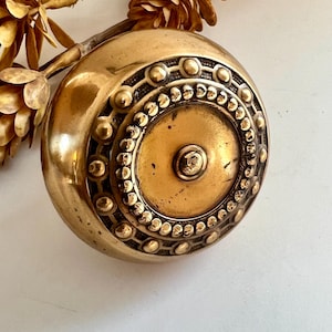 May include: A vintage brass doorknob with a circular design. The knob features a series of small, raised dots and a central medallion. The brass has a warm, golden hue, suggesting age and use. The doorknob is a classic piece of hardware.