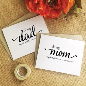 Puede incluir: Dos tarjetas blancas con caligraf&iacute;a negra. La tarjeta superior dice "Para mi pap&aacute; - mi modelo a seguir, en mi d&iacute;a de boda". La tarjeta inferior dice "Para mi mam&aacute; - mi mejor amiga, en mi d&iacute;a de boda".