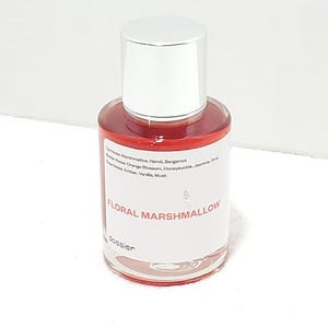 Puede incluir: Un peque&ntilde;o frasco de perfume con tap&oacute;n plateado y cuerpo de vidrio transparente. El l&iacute;quido interior es rojo vibrante. La etiqueta dice "FLORAL MARSHMALLOW". El frasco est&aacute; sobre una superficie blanca.