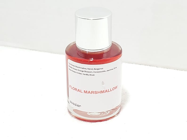 Puede incluir: Un peque&ntilde;o frasco de perfume con tap&oacute;n plateado y cuerpo de vidrio transparente. El l&iacute;quido interior es rojo vibrante. La etiqueta dice "FLORAL MARSHMALLOW". El frasco est&aacute; sobre una superficie blanca.