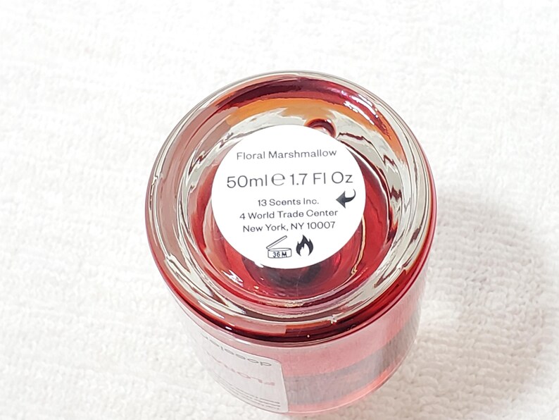 Puede incluir: Una botella de vidrio transparente con l&iacute;quido rojo en su interior. La etiqueta dice "Floral Marshmallow" y "50ml e 1.7 Fl Oz." La botella es de 13 Scents Inc., ubicada en Nueva York, NY. La parte inferior de la botella tiene un s&iacute;mbolo de advertencia.