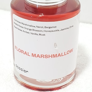 Puede incluir: Una botella de vidrio transparente llena de un l&iacute;quido rojo-anaranjado. La etiqueta dice "FLORAL MARSHMALLOW" con una lista de notas de fragancia: Malvavisco, Neroli, Bergamota, Flor de Naranja, Madreselva, Jazm&iacute;n, Lirio, &Aacute;mbar, Vainilla y Almizcle.