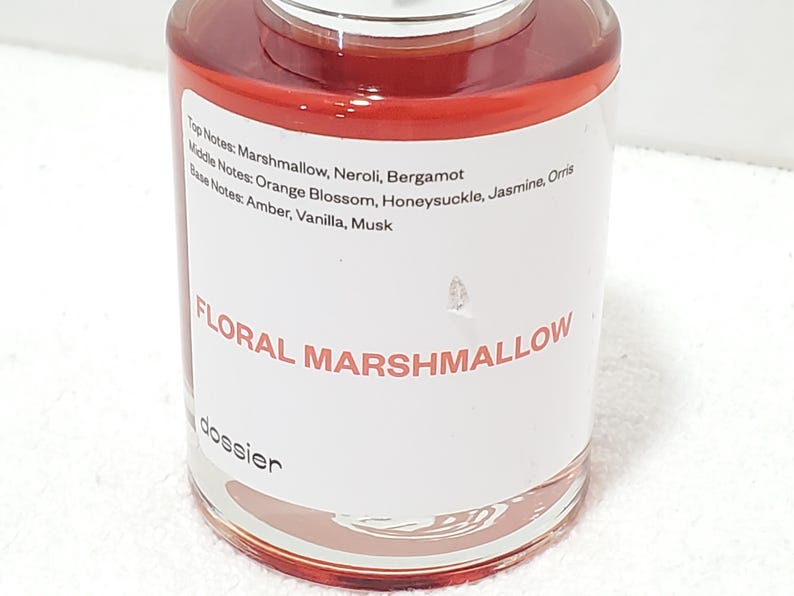 Puede incluir: Una botella de vidrio transparente llena de un l&iacute;quido rojo-anaranjado. La etiqueta dice "FLORAL MARSHMALLOW" con una lista de notas de fragancia: Malvavisco, Neroli, Bergamota, Flor de Naranja, Madreselva, Jazm&iacute;n, Lirio, &Aacute;mbar, Vainilla y Almizcle.