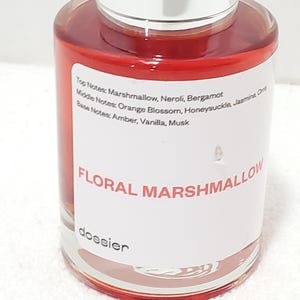 Puede incluir: Un frasco de perfume transparente con tapa plateada, lleno de un l&iacute;quido rojo-anaranjado. La etiqueta dice "FLORAL MARSHMALLOW" y enumera las notas de fragancia. La marca "dossier" tambi&eacute;n es visible.