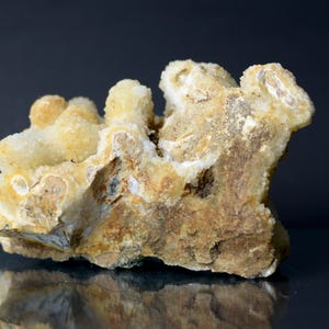 May include: A natural mineral specimen with a rough, textured surface. The rock formation features a mix of beige, brown, and off-white colors. The mineral has a crystalline structure with rounded, protruding formations.