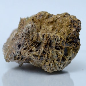 May include: A raw mineral specimen featuring a complex, crystalline structure with a rough, porous texture. The stone displays earthy tones of brown, tan, and ochre, with sharp, intersecting blade-like formations throughout its irregular surface.