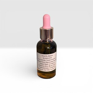 May include: A small, dark glass bottle of face oil serum with a pink dropper. The label lists ingredients including jojoba, sweet almond, and rosehip seed. The bottle has a silver cap and is set against a white background.