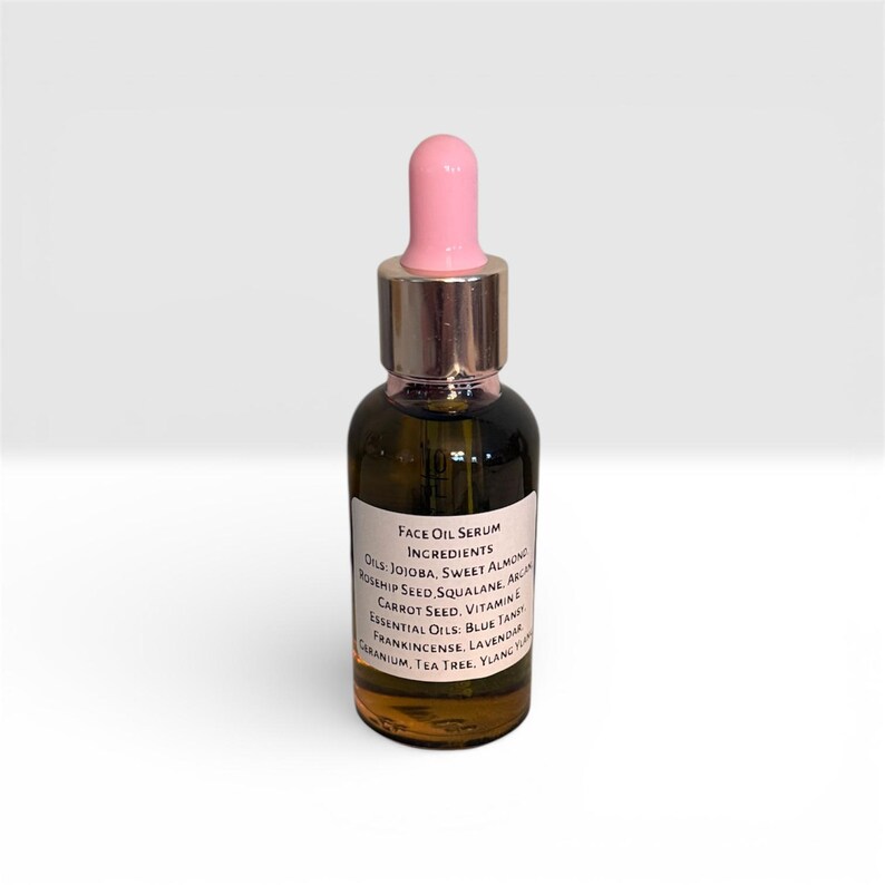 May include: A small, dark glass bottle of face oil serum with a pink dropper. The label lists ingredients including jojoba, sweet almond, and rosehip seed. The bottle has a silver cap and is set against a white background.