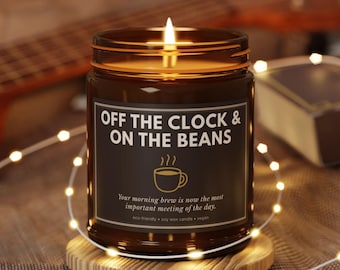 Może przedstawiać: Płonąca świeca sojowa w brązowym szklanym słoiku z czarną etykietą. Etykieta zawiera napis: OFF THE CLOCK & ON THE BEANS, ikonę filiżanki kawy oraz tekst: Your morning brew is now the most important meeting of the day. eco-friendly soy wax candle vegan.
