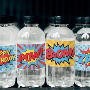 May include: Four clear plastic water bottles with colorful comic book themed labels. The labels say "Happy Birthday", "Pow!", "Boom!" and "Zap!"