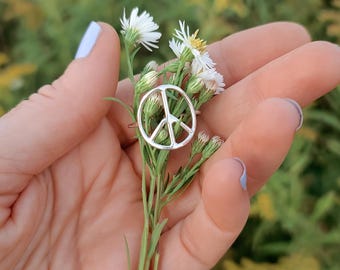 Könnte beinhalten: Ein silberner Friedenszeichenring an einer Hand, die einen Strauß weißer Wildblumen hält.
