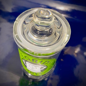 May include: A clear glass jar with a green and black label that says "GRIDIRON TRINKETS". The jar has a glass lid with a knob on top.