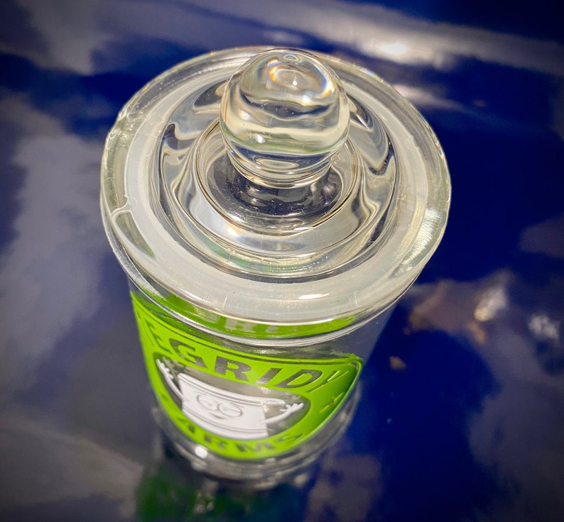 May include: A clear glass jar with a green and black label that says "GRIDIRON TRINKETS". The jar has a glass lid with a knob on top.