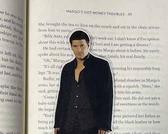Op de afbeelding: Een close-up van een boekpagina met een uitgesneden afbeelding van een man in een zwart pak en een zwarte kilt. De tekst op de pagina luidt "Margo's Got Money Troubles 59" en bevat dialogen uit het boek.