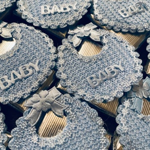May include: Blue and white baby bibs with the word "BABY" embroidered on each one. The bibs are made of a soft, crocheted fabric and are perfect for a baby shower or newborn gift.