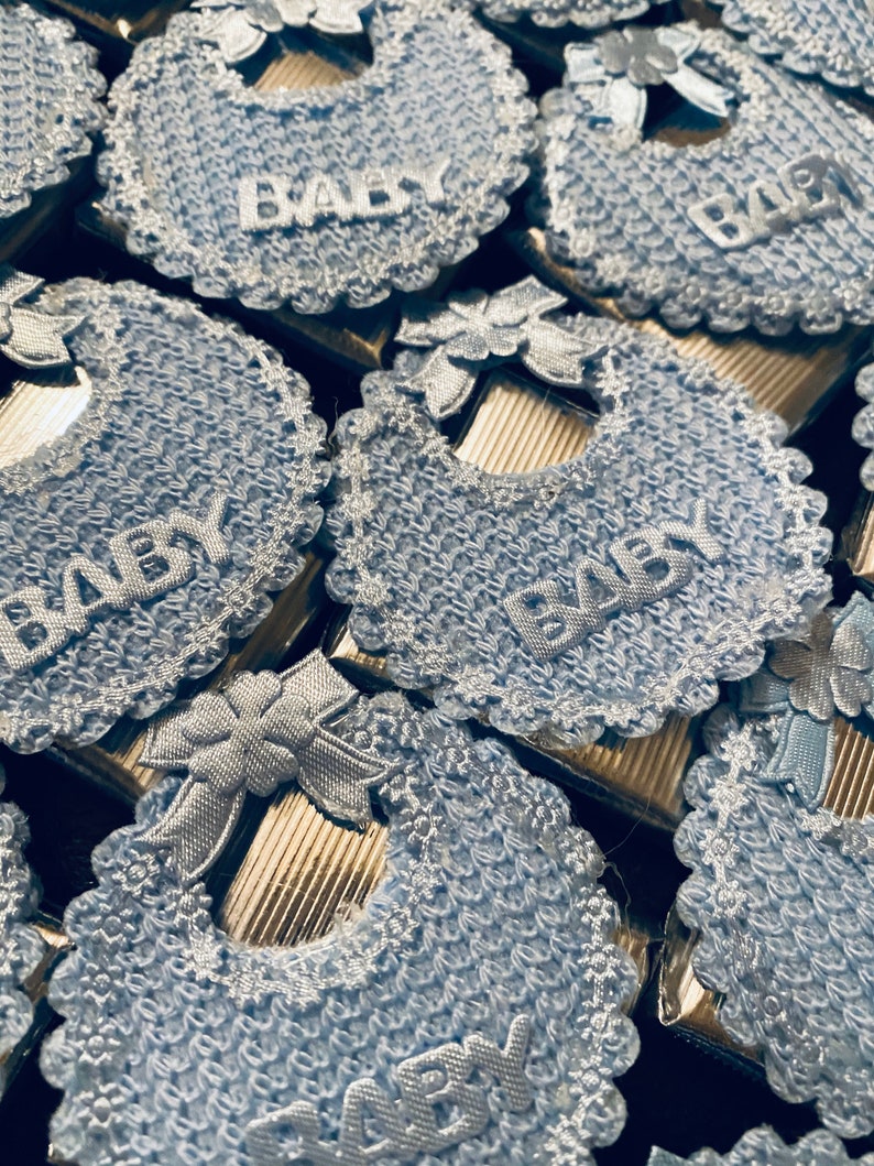 May include: Blue and white baby bibs with the word "BABY" embroidered on each one. The bibs are made of a soft, crocheted fabric and are perfect for a baby shower or newborn gift.