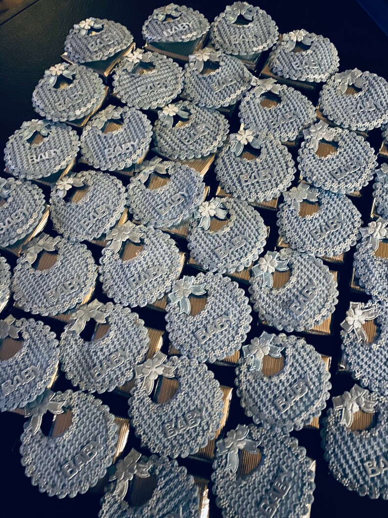 May include: A collection of blue and silver baby bib-shaped favors with the word "Baby" printed on each one.