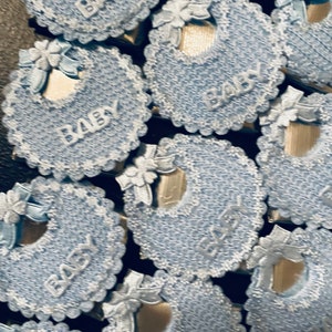 May include: A close-up of several blue and white baby bibs with the word "Baby" written on them. The bibs are made of a crocheted material and have a lace trim.