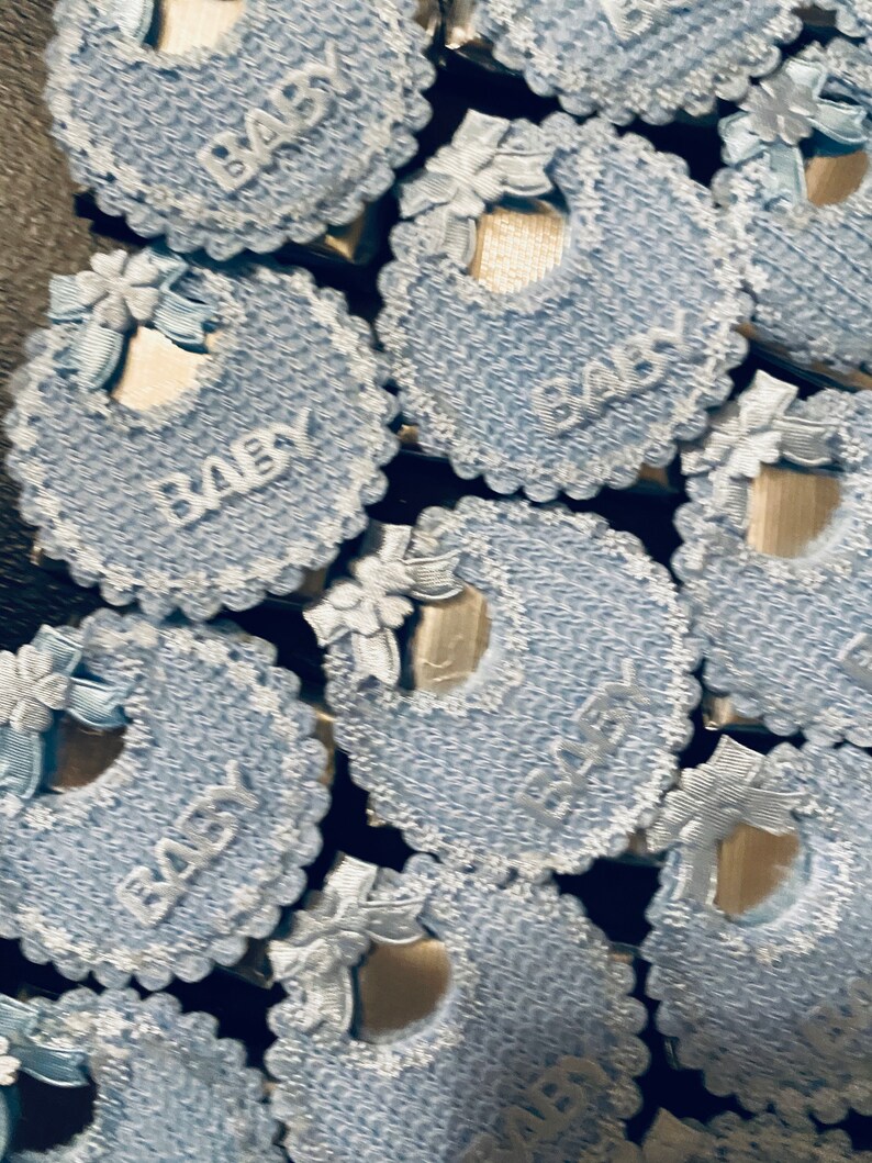 May include: A close-up of several blue and white baby bibs with the word "Baby" written on them. The bibs are made of a crocheted material and have a lace trim.