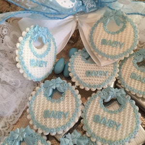 May include: A collection of blue and white baby bibs with the word "BABY" embroidered on each one. The bibs are decorated with blue bows and white lace.