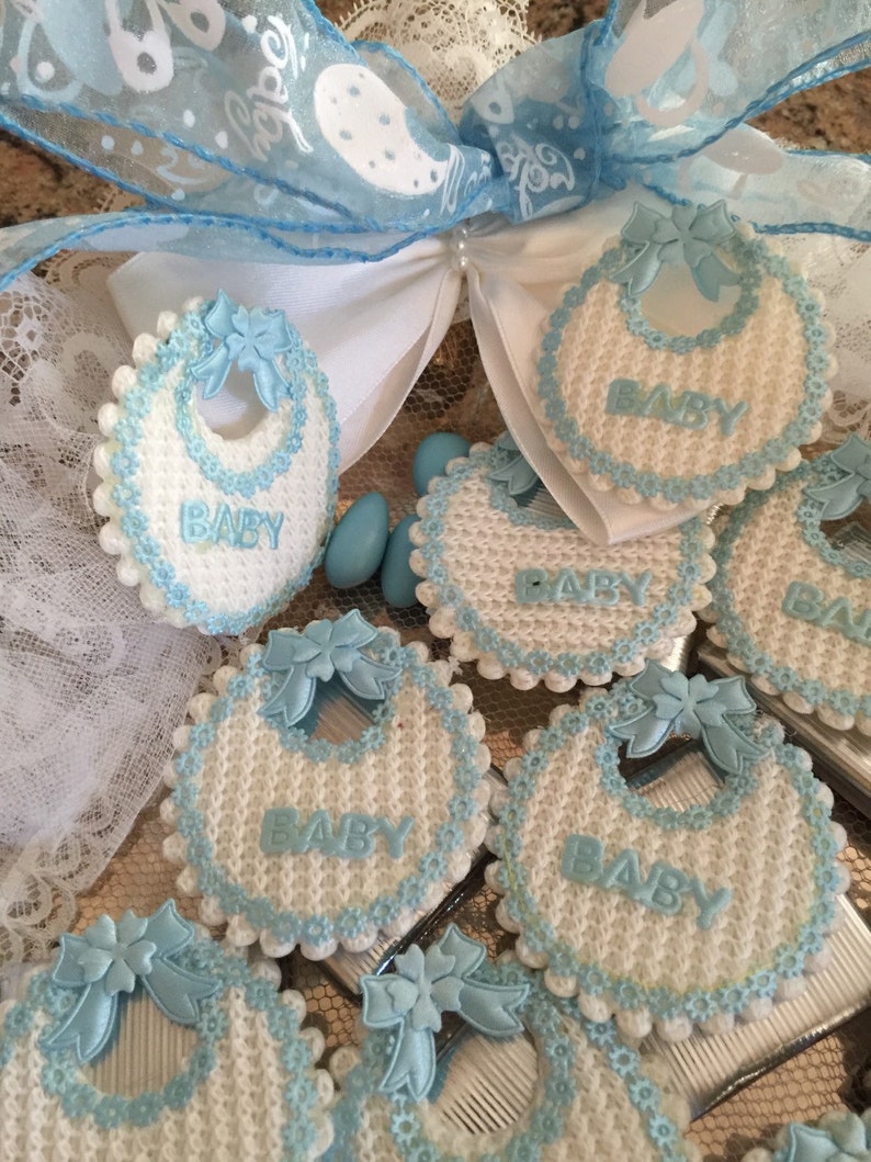May include: A collection of blue and white baby bibs with the word "BABY" embroidered on each one. The bibs are decorated with blue bows and white lace.