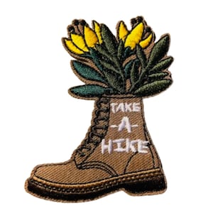 May include: Embroidered patch featuring a brown hiking boot with yellow flowers and green leaves coming out of the top. The boot has white text that reads "Take A Hike".