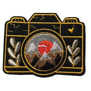 May include: Black and gold embroidered iron-on patch of a vintage camera with a mountain and sunset scene in the viewfinder.