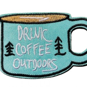 May include: A blue embroidered patch shaped like a coffee mug with the text "Drink Coffee Outdoors" and two small pine trees on either side of the text.