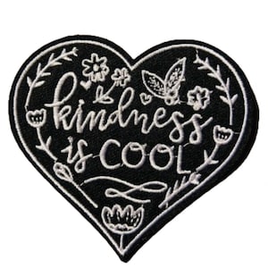 May include: Black heart-shaped embroidered patch with white stitching. The patch features the text "kindness is cool" surrounded by floral designs.