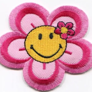 May include: A pink flower with a yellow smiley face in the center. The flower has a small pink flower on top.