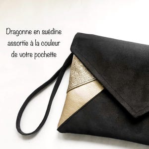 K&ouml;nnte beinhalten: Schwarze Clutch aus Wildleder mit einem goldenen und cremefarbenen Lederklappen. Die Clutch hat einen schwarzen Riemen.