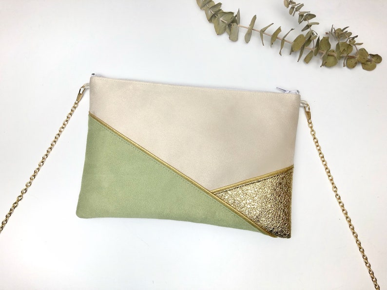K&ouml;nnte beinhalten: Eine beige, gr&uuml;ne und goldene Clutch mit einem goldenen Kettenriemen. Die Clutch hat ein geometrisches Design mit einem goldenen Akzent.