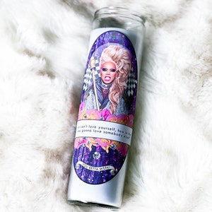 May include: A white glass candle with a purple, pink, and white design featuring a portrait of a drag queen with blonde hair and the text "You can't love yourself, how in the world you gonna love somebody else?" and "You Betta Werk!"