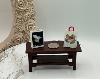 May include: Two miniature white paper shopping bags on a small wooden table. One bag has a dove with the word "PEACE" printed on it. The other bag has a colorful illustration of wrapped gifts.