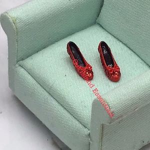 May include: A pair of red sparkly shoes with black heels sitting on a light green armchair.